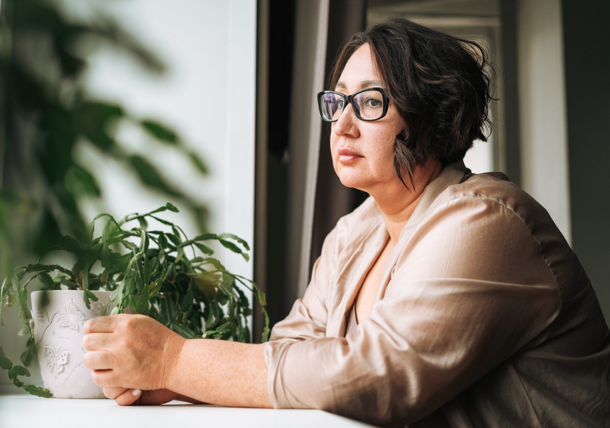 A sad woman gazing forward near a window.